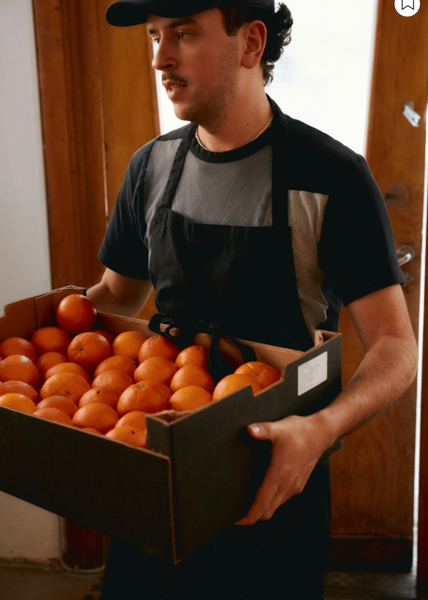 Kitchen staff member carrying a crate of oranges.