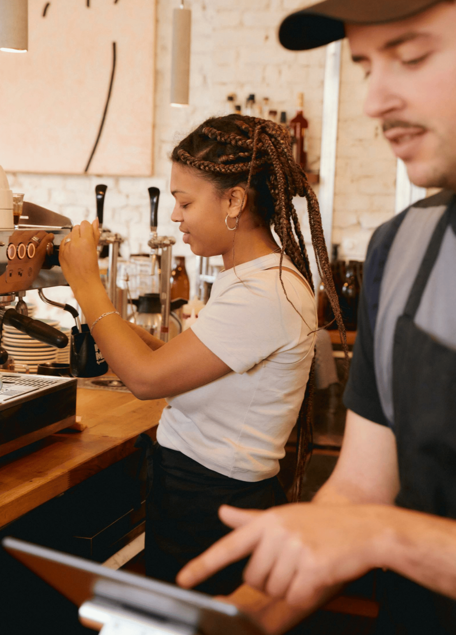 Cafe staff working beside a tablet and espresso machine.